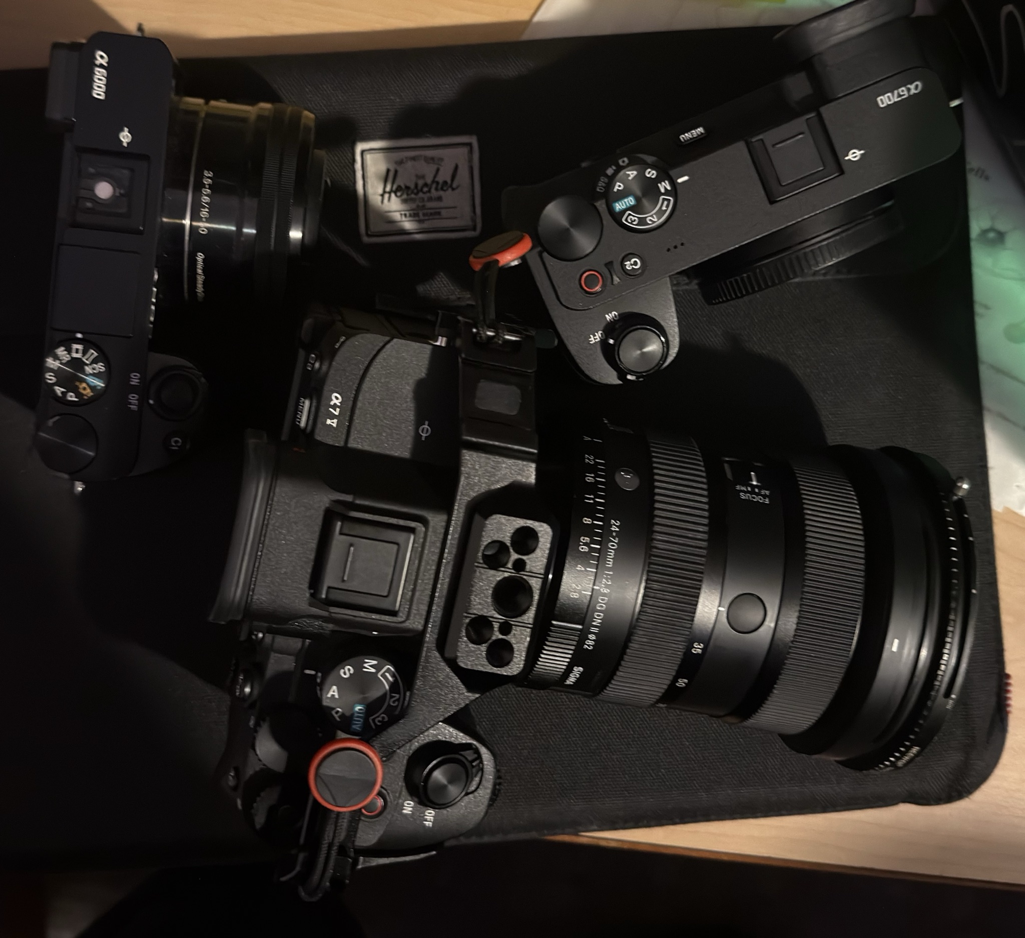 Sony α7 V with the Sigma 24–70mm lens, a Sony α6700 and a Sony α6000 with its 16–50mm lens, laid out on a dark mat